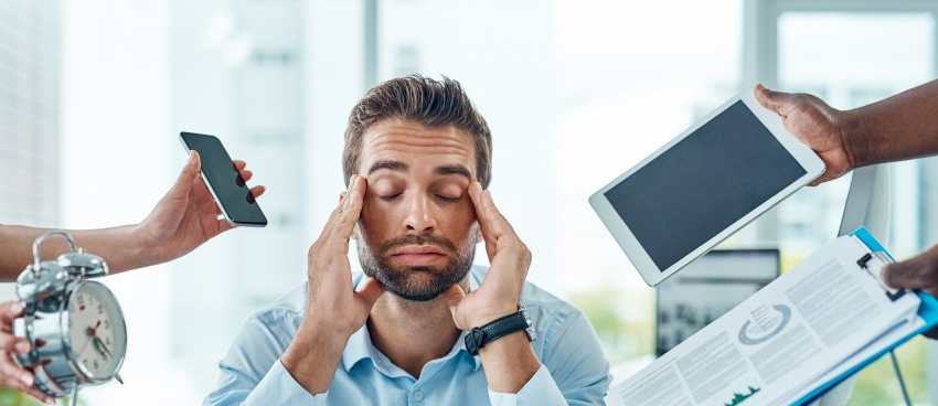 A close-up of a person holding their head in frustration, with a cluttered desk and multiple devices, visually representing stress and mental overload.